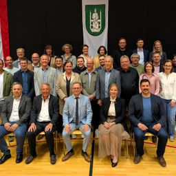 Ein Gruppenfoto von Männern und Frauen in formeller Kleidung, die in Reihen sitzen und stehen. Der Ort scheint ein Innenbereich zu sein, wahrscheinlich ein Tagungs- oder Veranstaltungsort.