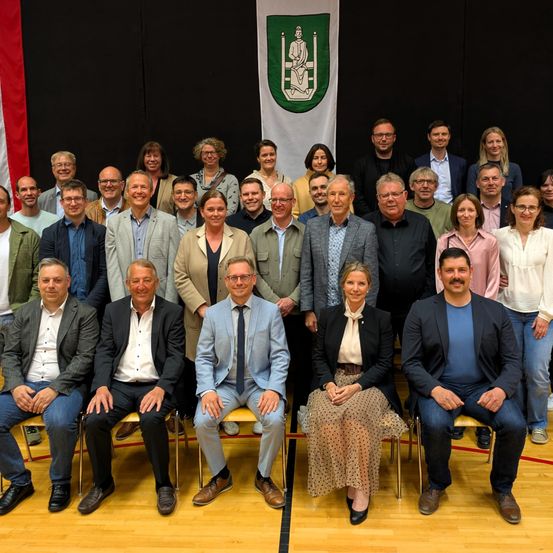 Ein Gruppenfoto von Männern und Frauen in formeller Kleidung, die in Reihen sitzen und stehen. Der Ort scheint ein Innenbereich zu sein, wahrscheinlich ein Tagungs- oder Veranstaltungsort.
