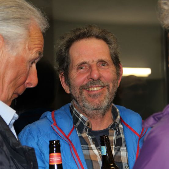 Drei Menschen lächeln in die Kamera. Der Mann in der Mitte hält eine Flasche.