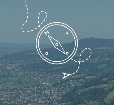 Ein Luftbild einer Stadt mit Bergen, einer Kompassnadel und einer gepunkteten Linie, die nach Norden führt. Der Kompass ist weiß mit einer roten Pfeilspitze.