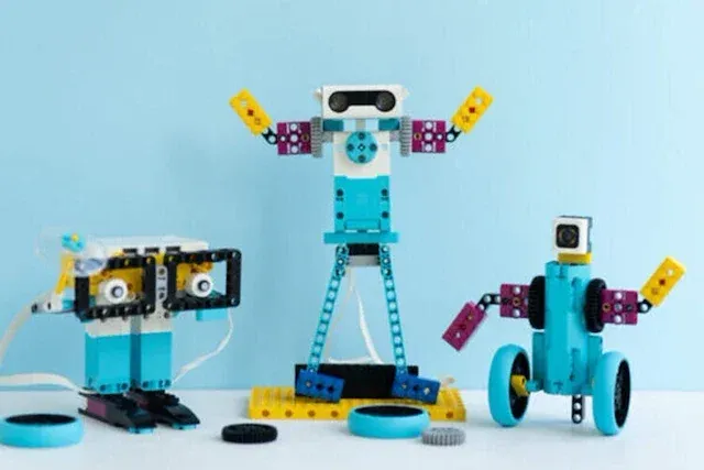 Drei Lego-Roboter in verschiedenen Designs und Farben sind vor einem hellblauen Hintergrund ausgestellt. Die Roboter bestehen aus mehreren Lego-Teilen, von denen jeder einzigartige Merkmale wie Räder, Zahnräder und Sensoren aufweist.