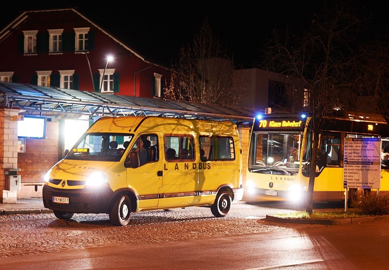 Zwei gelbe Landbus-Fahrzeuge sind nachts vor einem roten Gebäude geparkt. Der erste Bus hat den Text LANDBUS WEST an der Seite.