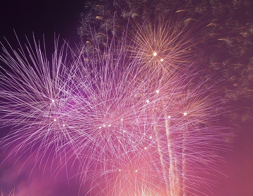 Ein lebhaftes Feuerwerk beleuchtet den Nachthimmel mit einer Palette aus rosa und weißen Farben.