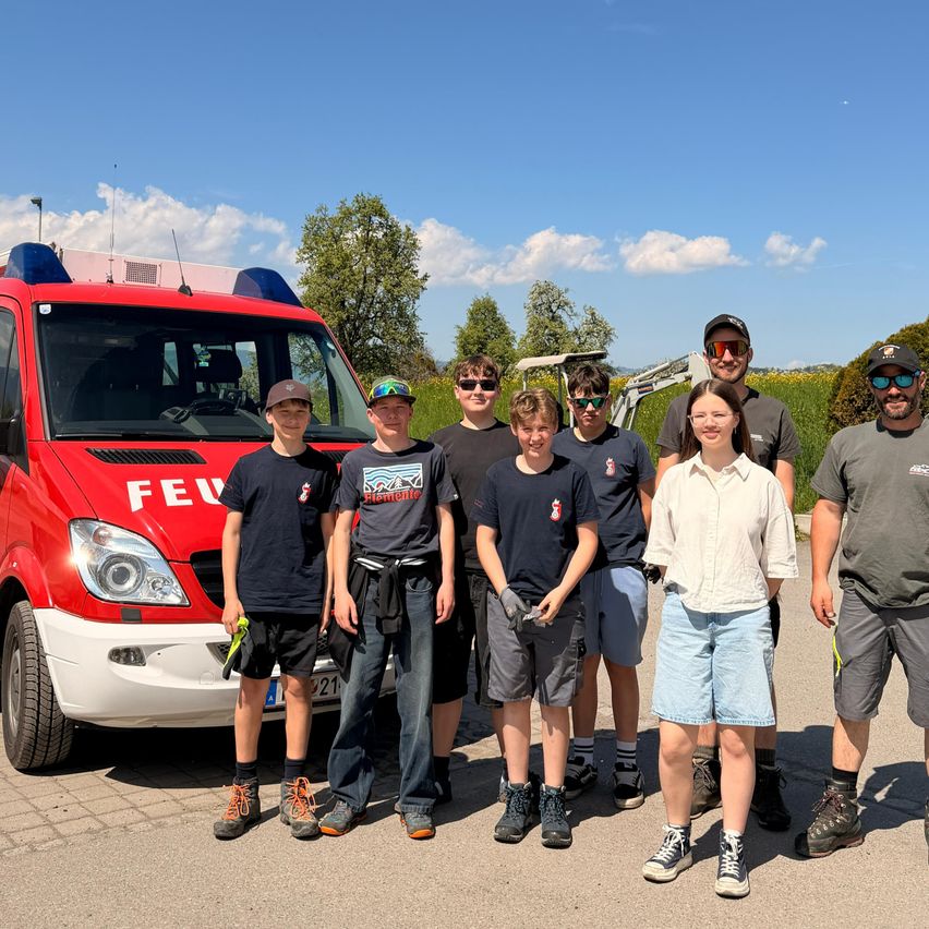 Eine Gruppe von Menschen, darunter junge Jungen und Mädchen, posiert für ein Foto vor einem roten Feuerwehrauto an einem sonnigen Tag.
