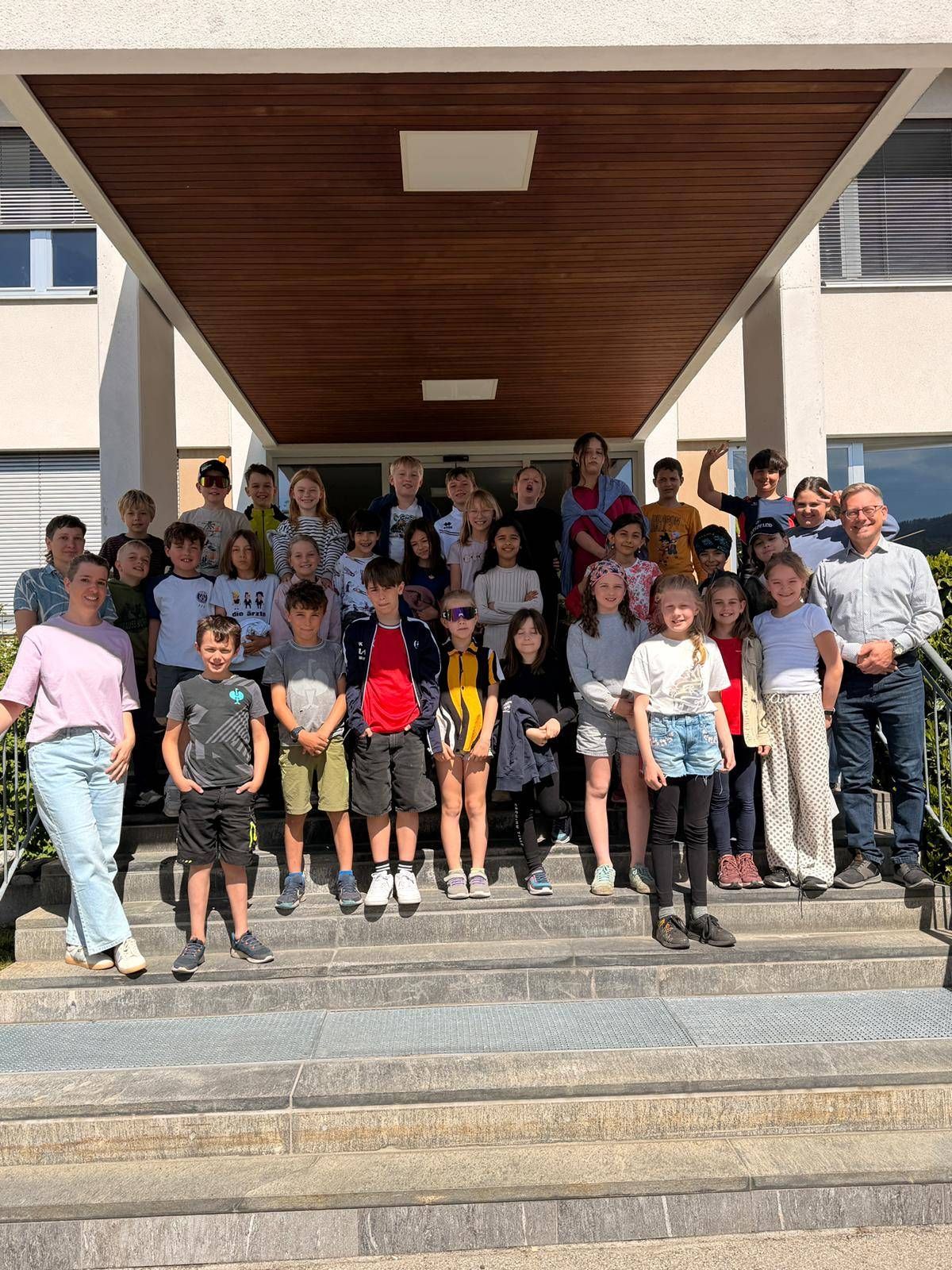 Eine Gruppe von Kindern und Erwachsenen posiert für ein Foto auf den Stufen eines Gebäudes. Die Kinder tragen Freizeitkleidung, und die Erwachsenen stehen oben und unten auf den Stufen.