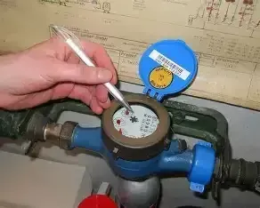 Eine Hand hält einen Stift und markiert einen Wasserzähler mit einem blauen Deckel und einem blau-weißen Körper. Der Zähleranzeiger ist mit einem roten Aufkleber versehen.