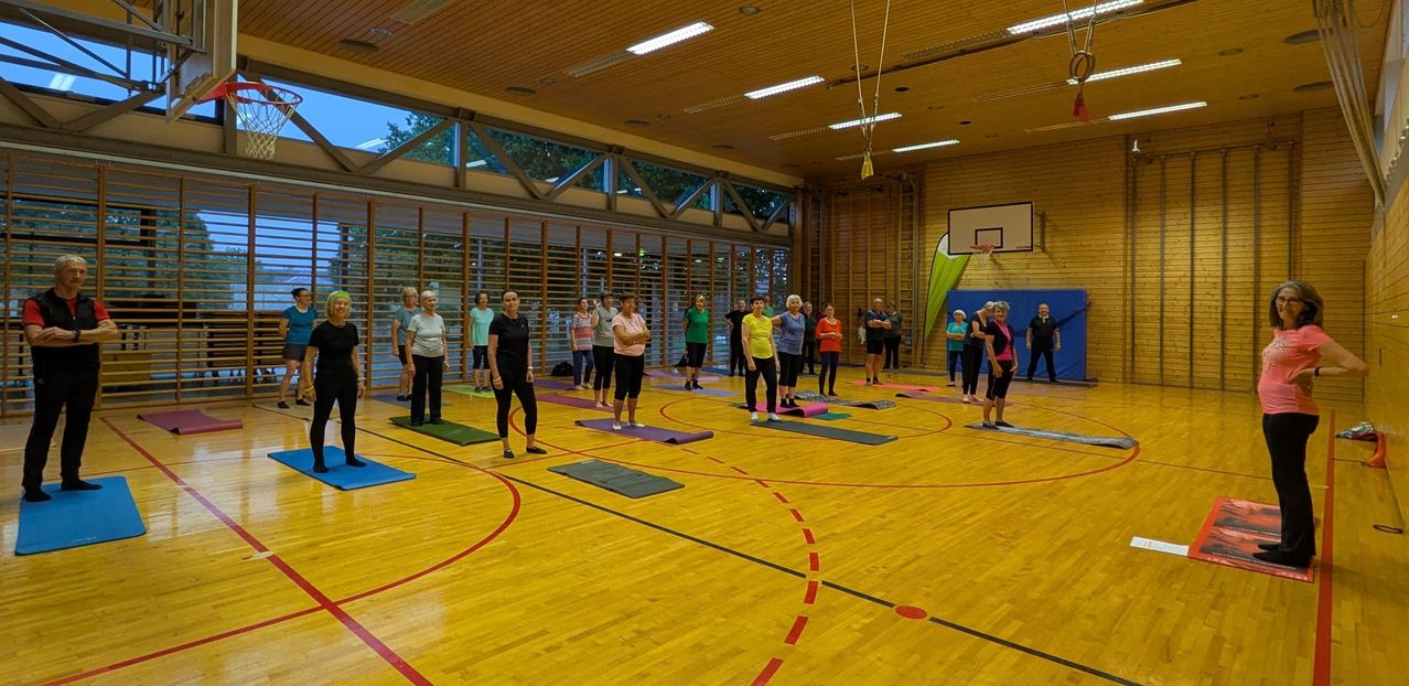 Eine Gruppe von Menschen in einem Fitnessstudio praktiziert Yoga auf Matten, mit einem Basketballkorb im Hintergrund.