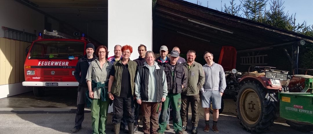 Eine Gruppe Erwachsener steht vor einem Gebäude mit einer weißen Wand und einem Dach mit Lichtern. Sie tragen alle Jacken, Hosen und Schuhe.