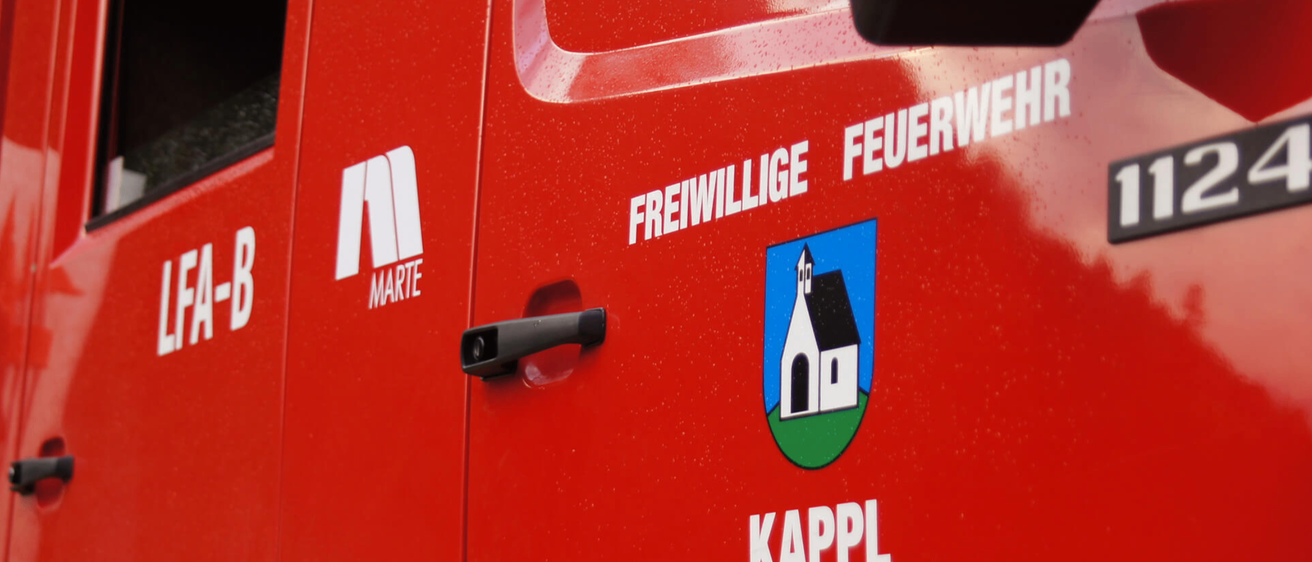 Ein Nahaufnahme einer roten Fahrzeugtür mit dem Text 'Freiwillige Feuer' und einem Logo mit einer Kirche. Darunter steht 'KAPPL'. Der Türgriff ist schwarz.