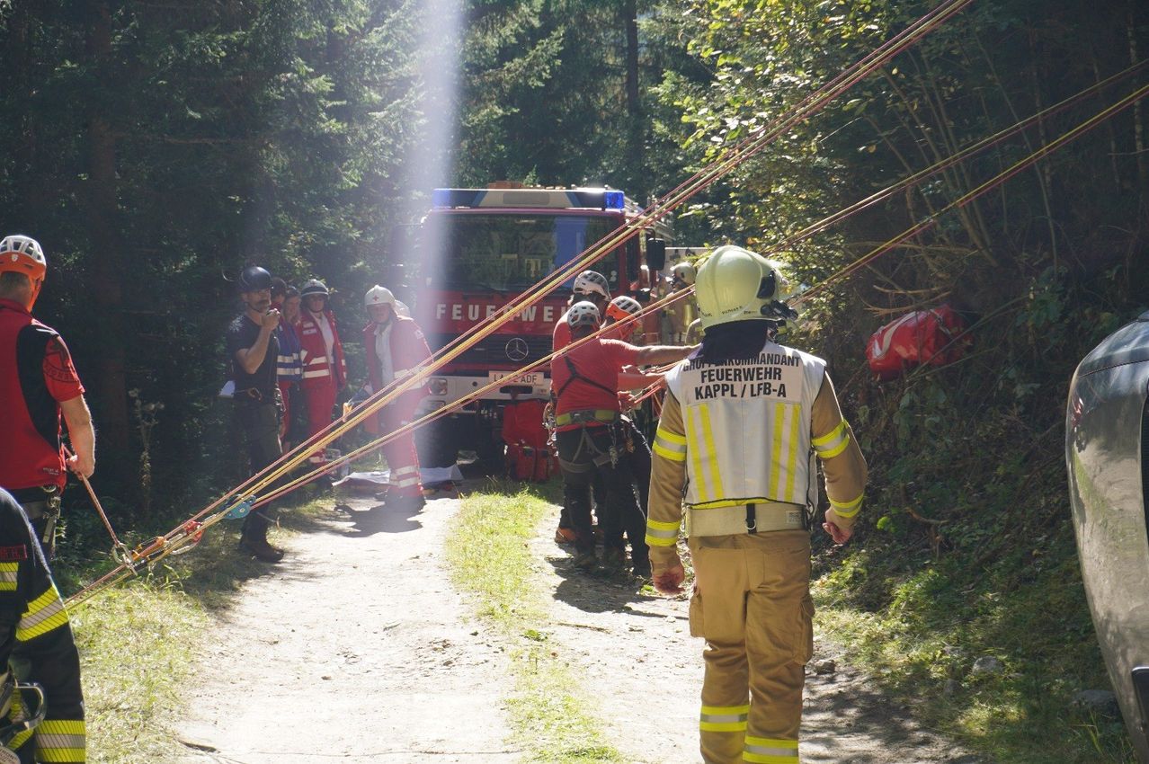 Feuerwehrleute in roten und weißen Uniformen bereiten sich auf eine Rettung vor, mit einem Feuerwehrwagen im Hintergrund.