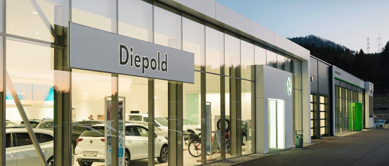 Das Äußere eines modernen Diebold-Autohauses zeigt ein klares Design mit großen Glasfenstern, die Autos im Inneren präsentieren. Der Name Diebold ist deutlich auf einem Schild über dem Eingang angebracht.