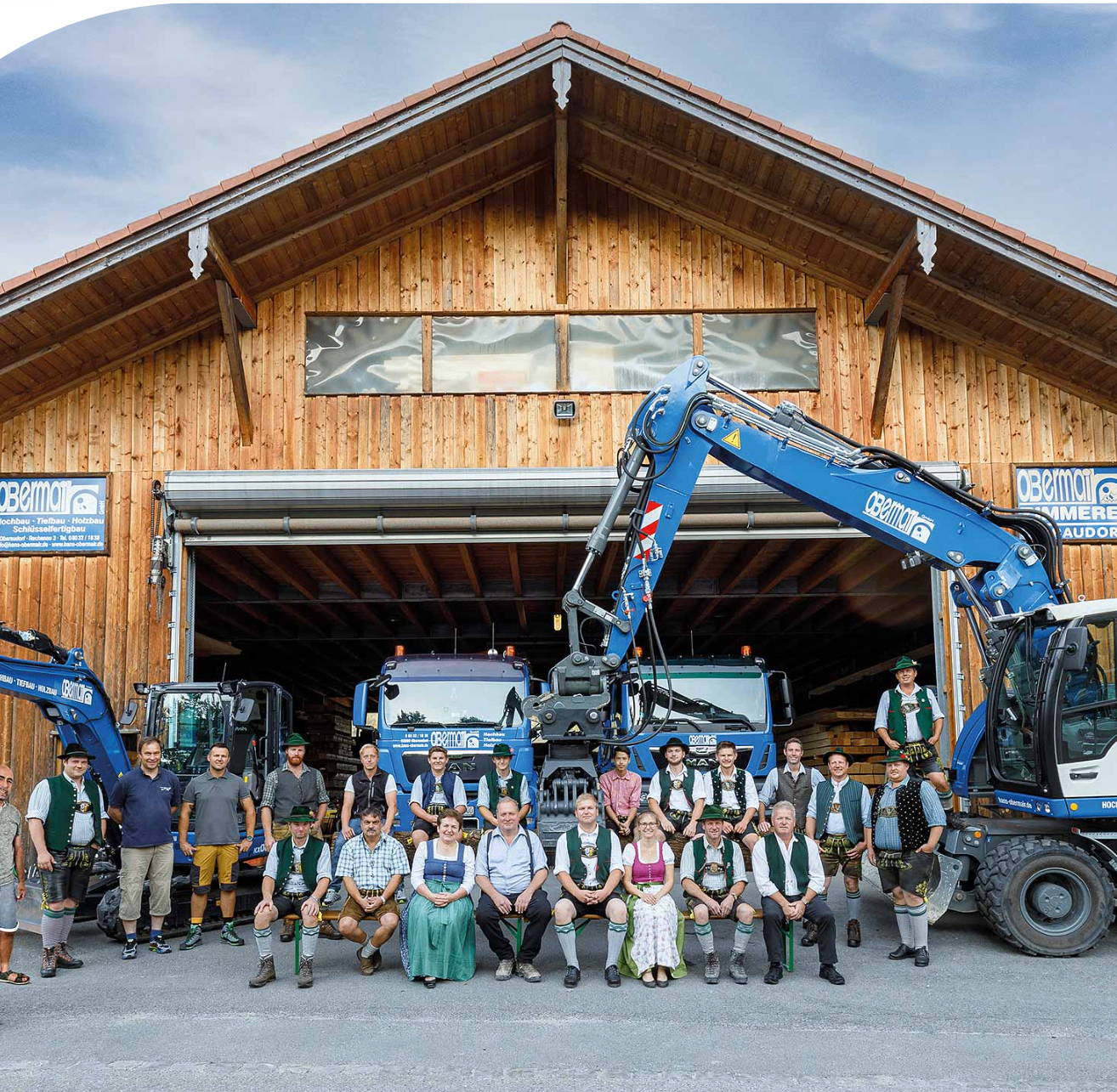 Eine Gruppe von Menschen in traditioneller Kleidung posiert vor einem Holzgebäude mit schwerem Gerät im Inneren.