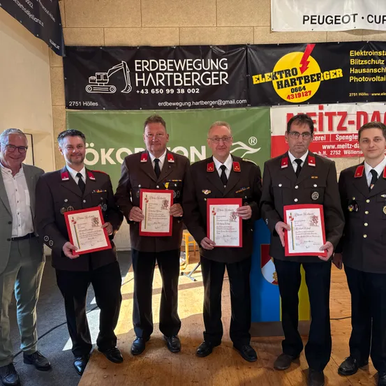 Fünf Männer in Uniformen mit Urkunden stehen in einer Gruppe vor einem Banner mit den Worten Elektro Hartberger.