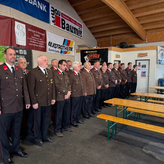 Eine Gruppe uniformierter Personen steht in einer Reihe, wahrscheinlich bei einer formellen Veranstaltung. Sie tragen Medaillen und stehen vor einem Banner.