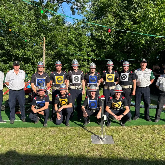 Eine Gruppe Feuerwehrleute in Uniformen und Helmen posiert für ein Foto auf einem grünen Feld.