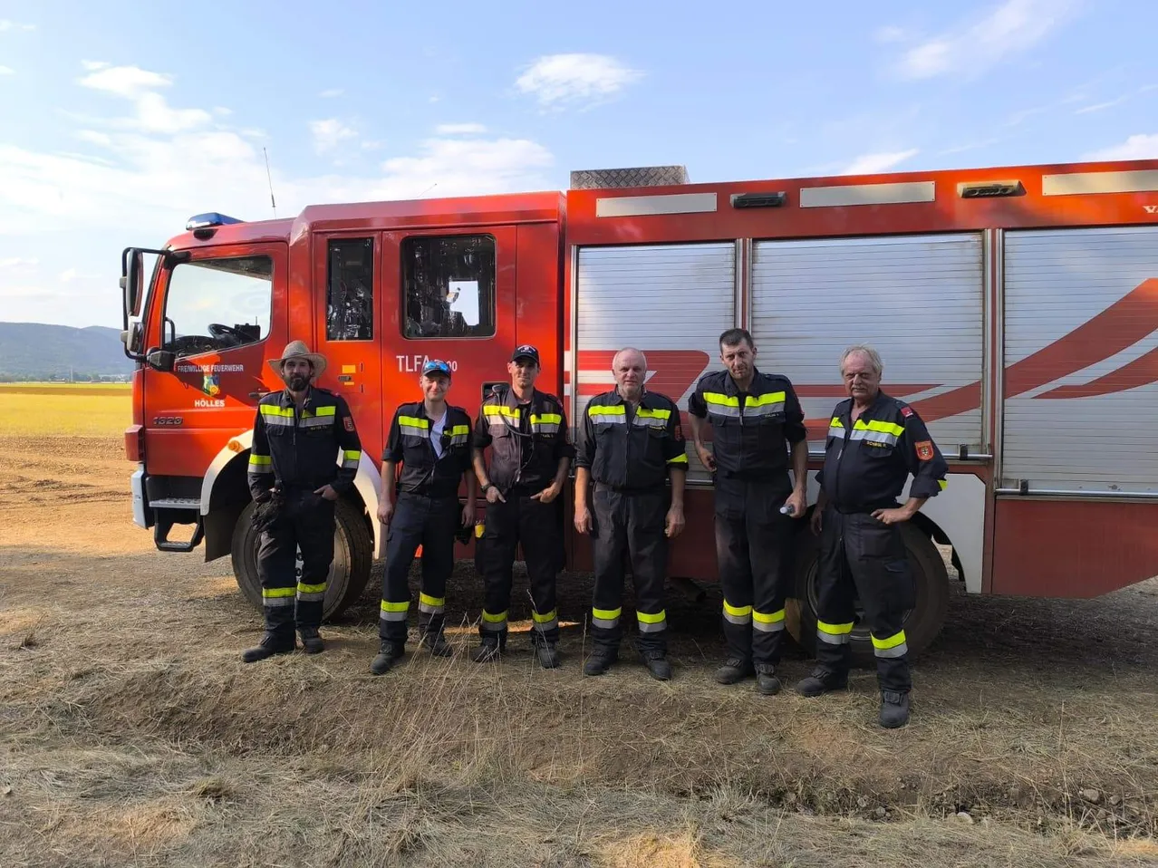 Eine Gruppe von Feuerwehrleuten in Uniform steht vor einem roten Feuerwehrauto mit der Aufschrift TLF 400 an der Seite. Sie posieren für ein Foto auf einem Feld.