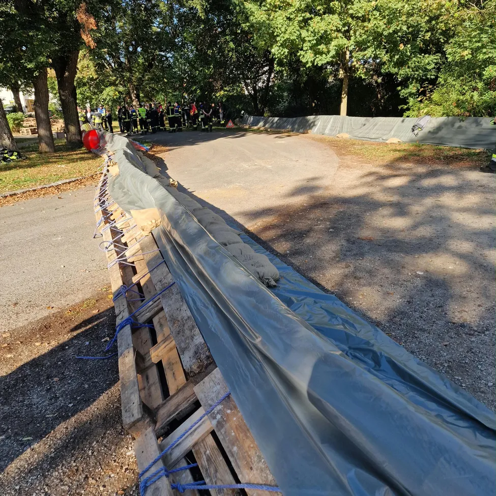 Eine Straße mit einer temporären Barriere aus Holzpaletten und blauer Plane, mit Menschen in gelben Westen in der Nähe.
