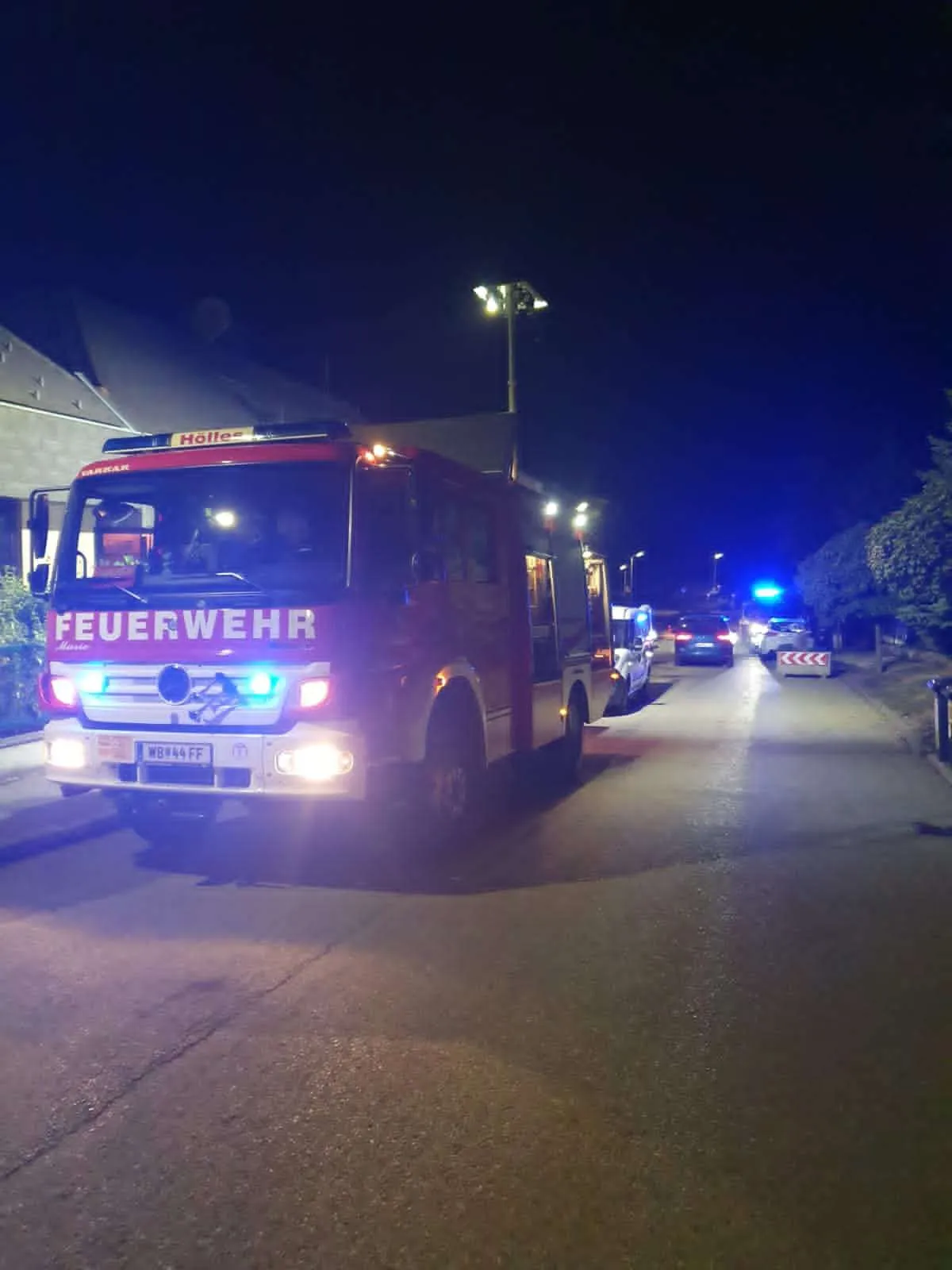 Ein roter Feuerwehrwagen mit eingeschalteten Lichtern fährt nachts die Straße entlang.