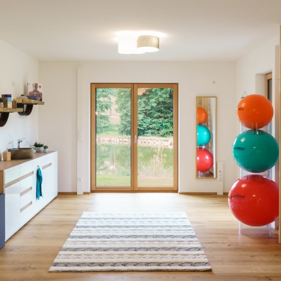 Ein leerer Raum mit Holzboden und weißen Wänden. Eine Teppich liegt in der Mitte. Rechts befinden sich große bunte Bälle.