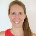 Eine Frau mit langen braunen Haaren lächelt in die Kamera. Sie trägt ein rotes ärmelloses Oberteil und hat ein Muttermal auf ihrer linken Wange.