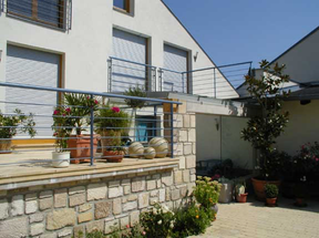 Ein modernes Haus mit Balkon hat eine Steinmauer und einen Balkon mit Geländer. Es gibt Topfpflanzen und Blumen auf dem Balkon und im Hof.