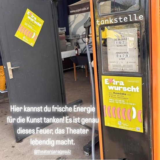 Eine orangefarbene Zapfsäule mit dem Wort 'kleinkunst' darauf. Ein gelbes Plakat mit den Worten 'Extra wurst' ist an der Zapfsäule befestigt. Eine Tür ist offen, und ein Plakat ist daran befestigt. Ein Tisch mit einer Flasche und einer Tischdecke befindet sich im Raum. Ein Vorhang hängt an der Wand.