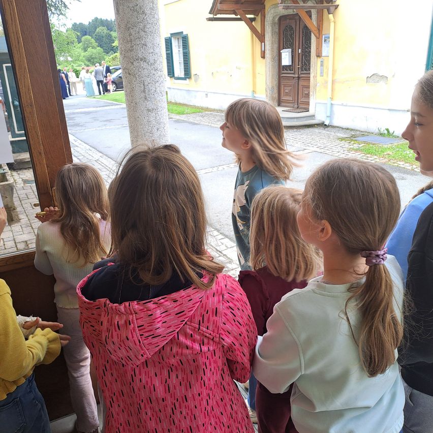 A group of young girls are standing outside near a building. They appear to be looking at something in the distance.