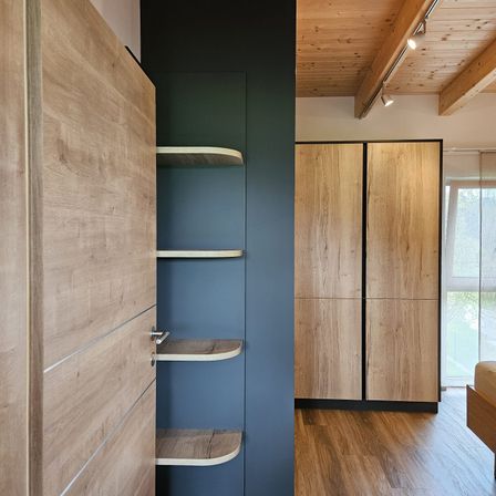 Ein modernes Interieur zeigt einen Holzschrank mit Regalen, einer blauen Wand und einem Holzboden. Der Raum hat eine gemütliche Atmosphäre.