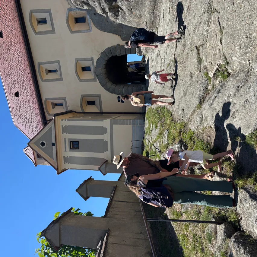 Eine Gruppe von Menschen mit Hüten steht auf einem Felsen vor einem Gebäude. Sie scheinen die Gegend zu erkunden.