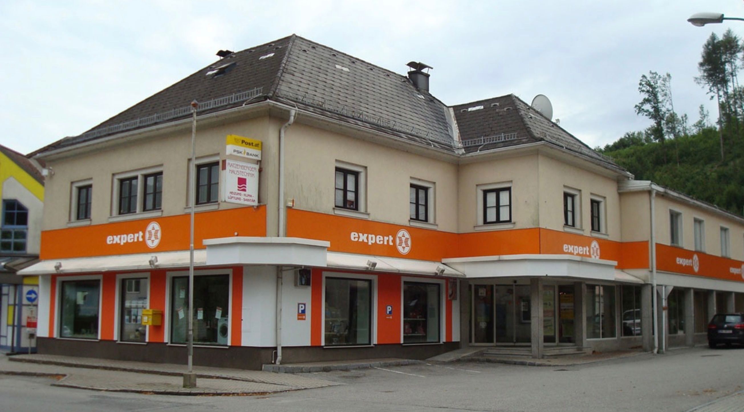 Ein zweistöckiges Gebäude mit orange-weißer Außenfassade. Es hat ein Schild mit der Aufschrift 'expert' in der Mitte, mehrere Fenster und einen Schornstein oben.