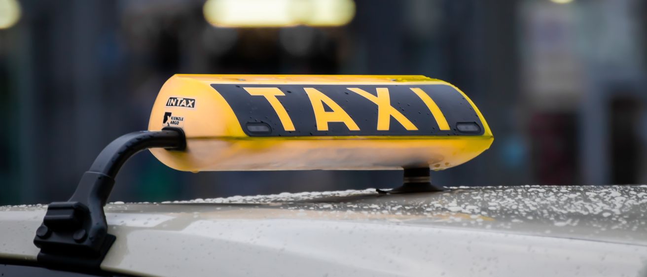 Eine Nahaufnahme des gelben Taxi-Schildes an einem regnerischen Tag. Das Schild zeigt das Wort TAXI, mit INTAX und dem Wort ARCG.