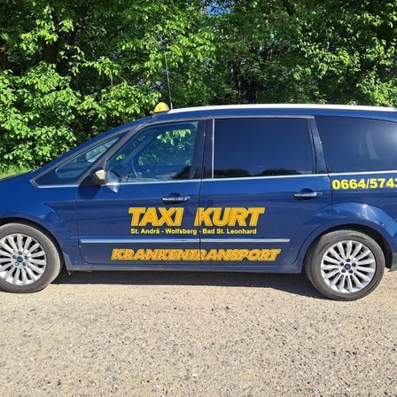 Ein blauer Ford S-MAX Van mit Taxi-Service-Werbung steht auf einer Schotterstraße mit Bäumen im Hintergrund. Die Nummer 0664/574 ist auf der Seite sichtbar.