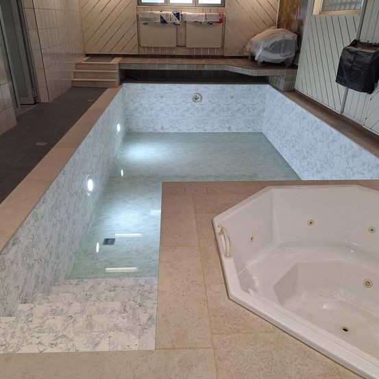 Ein leerer Marmorpool mit Glasseiten und einer Whirlpool auf der rechten Seite. Der Pool hat einen Abfluss und Lichter am Boden.