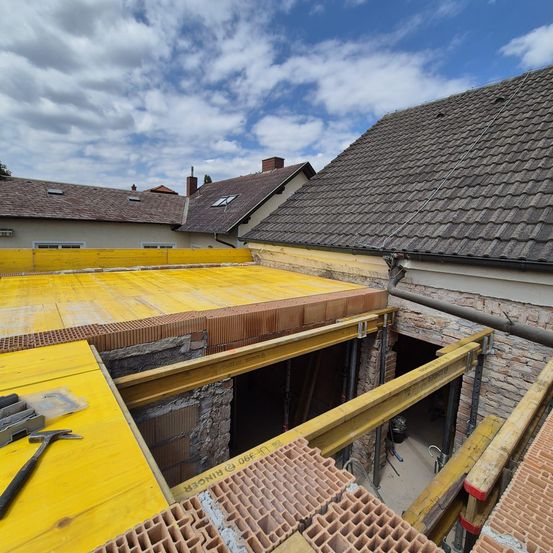 Ein Baustellenbild zeigt ein Haus in Renovierung mit gelben Gerüsten und einem neuen gelben Dach. Ein Hammer ist links.