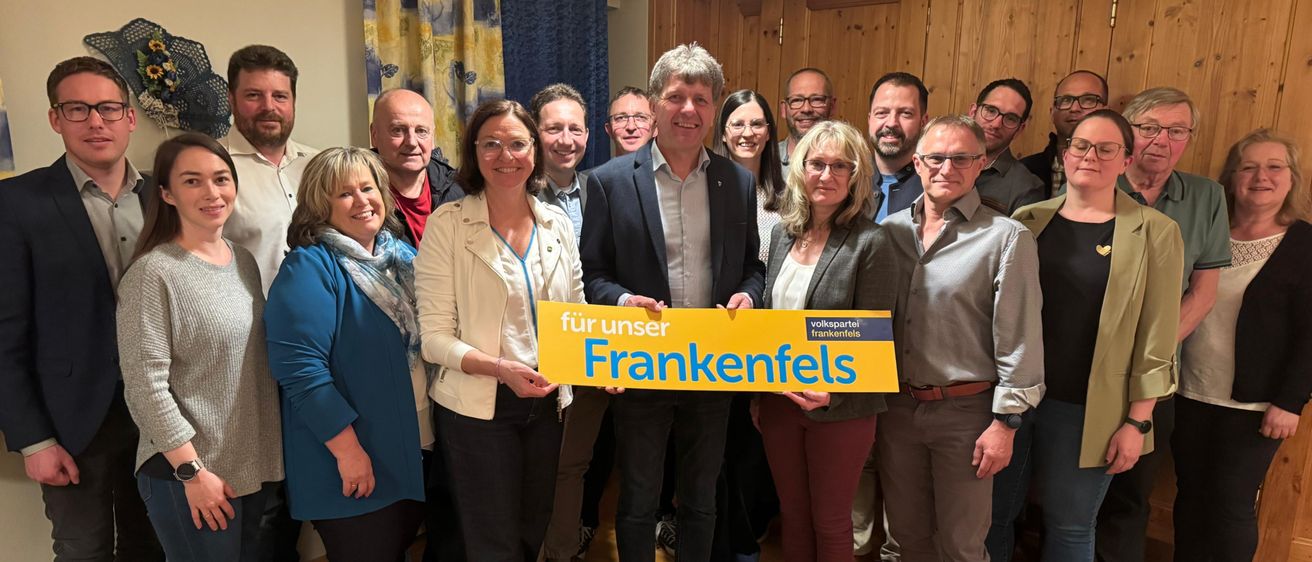 Eine Gruppe von Menschen posiert für ein Foto in einem Raum. Zwei Frauen halten ein gelbes Banner, auf dem 'für uns Frankenfels' steht. Dahinter lächeln zwei Männer.
