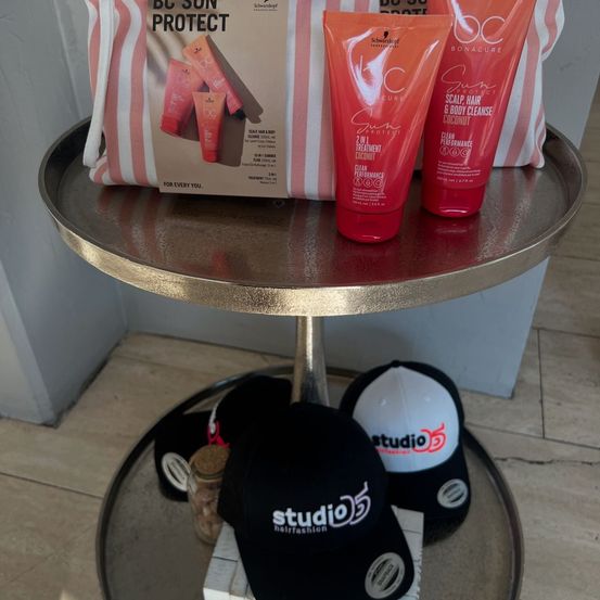 Eine Präsentation von Schönheitsprodukten auf einem Tisch, darunter eine BC Sun Protect-Tasche, zwei Sonnenschutzflaschen und zwei Studio 55-Kappen.