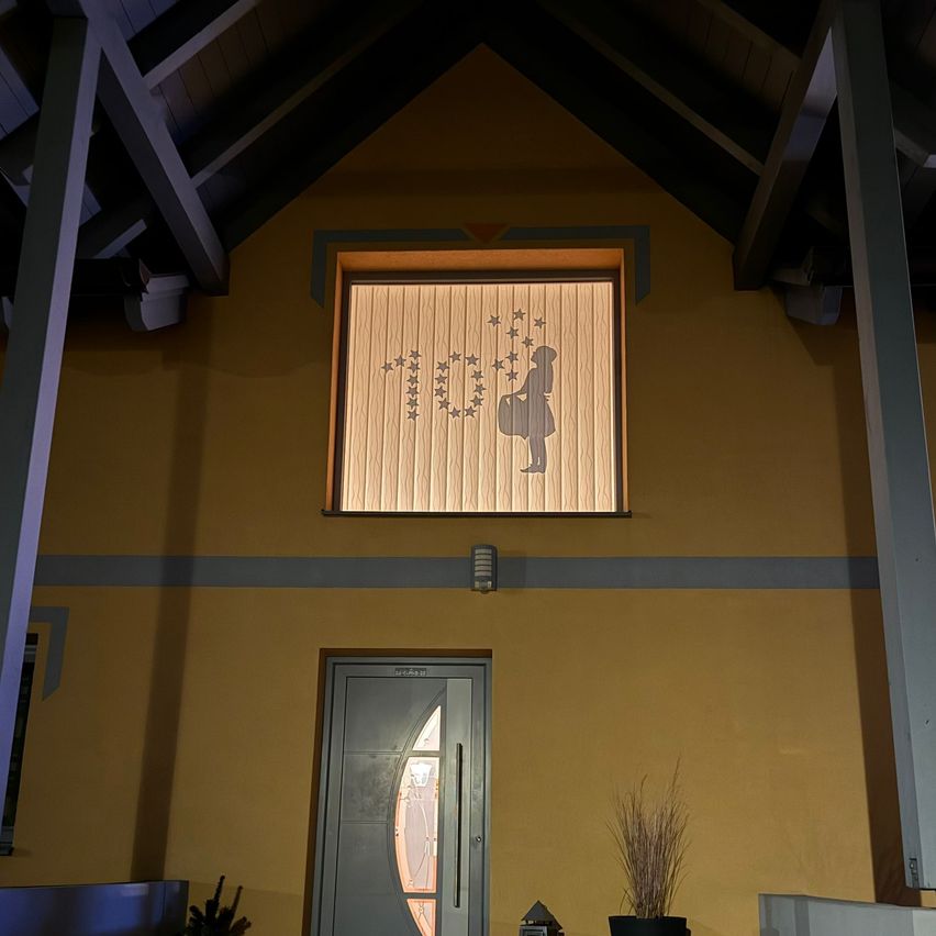 A yellow building with a window featuring a silhouette of a girl carrying a bag and stars above. Below the window is a gray door with a glass window.