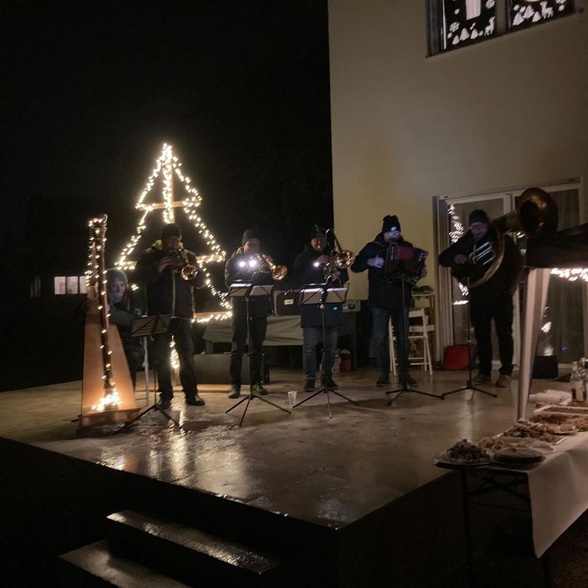 Eine Gruppe Musiker tritt bei Nacht auf einer Bühne auf, mit einem beleuchteten Weihnachtsbaum und Dekorationen im Hintergrund.