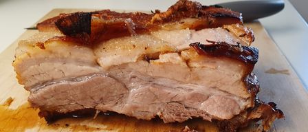 A close-up of a sliced pork belly on a wooden cutting board, with crispy skin and juicy meat.