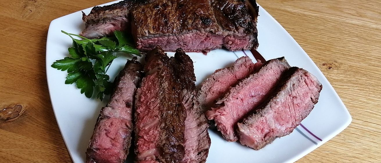 Ein weißer Teller mit perfekt gegrilltem Steak und Scheiben, mit Petersilie garniert, auf einem Holztisch.