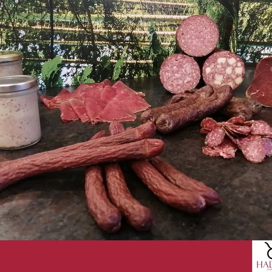 Eine Auswahl verschiedener Würste, einschließlich Salami, Salami-Scheiben und einem Glas Dressing, auf einem Tresen zusammengestellt.