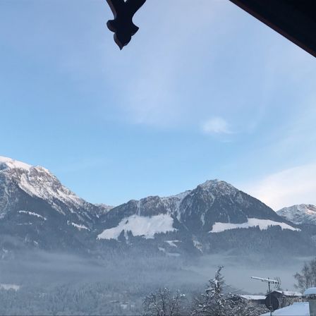 Eine Gebirgslandschaft mit schneebedeckten Gipfeln und Tälern unter einem klaren blauen Himmel mit einigen Wolken.