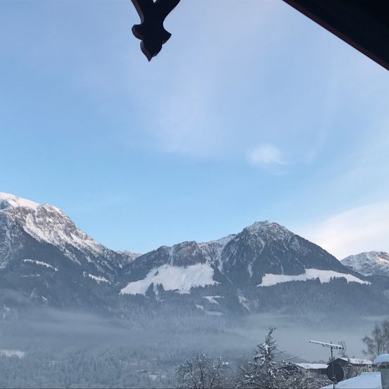 Eine Gebirgslandschaft mit schneebedeckten Gipfeln und Tälern unter einem klaren blauen Himmel mit einigen Wolken.