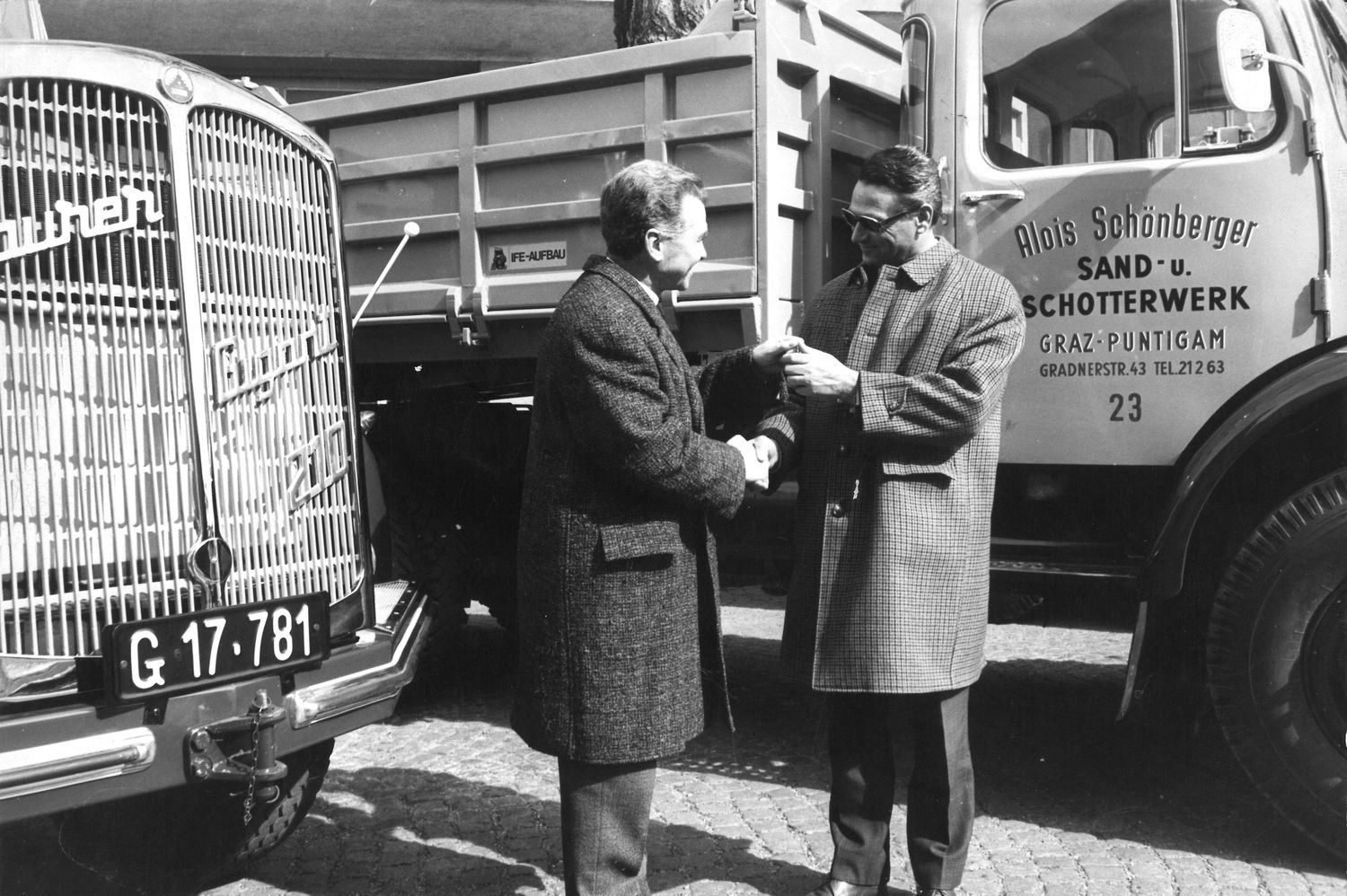 Zwei Männer schütteln sich die Hände vor Lastwagen. Ein Lastwagen heißt Alois Schott.