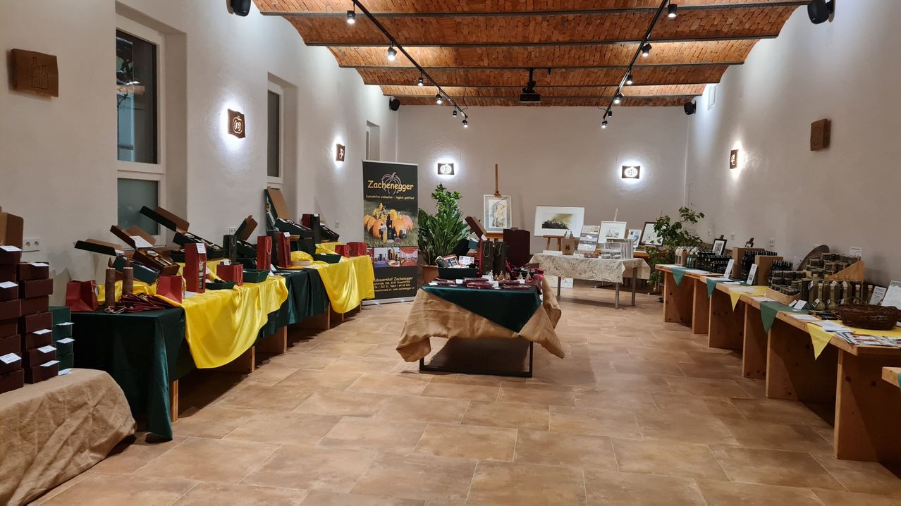 Ein Raum mit mehreren mit Tischdecken bedeckten Tischen, auf denen Gegenstände wie Flaschen, Taschen und Kunstwerke ausgestellt sind. Es hat eine Holzdecke mit Lichtern und Wanddekorationen.