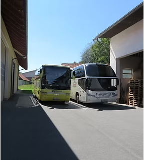 Two buses, one yellow and one white, are parked on the side of a road near a building with a garage.