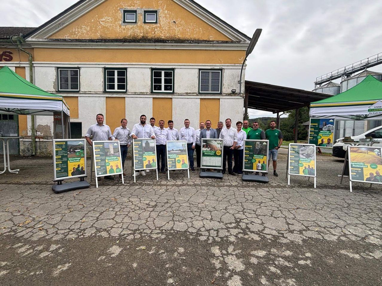 Eine Gruppe von Menschen in weißen Hemden posiert vor einem Gebäude mit Bannern auf einem rissigen Boden.