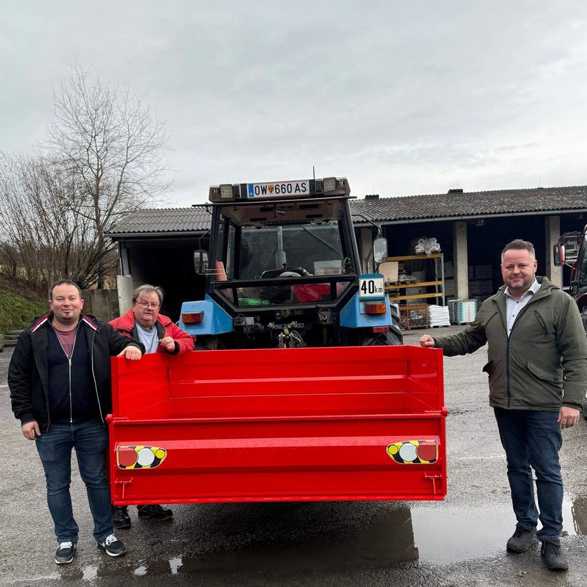 Drei Männer stehen neben einem roten Traktor mit der Nummer 40 vor einem Gebäude.