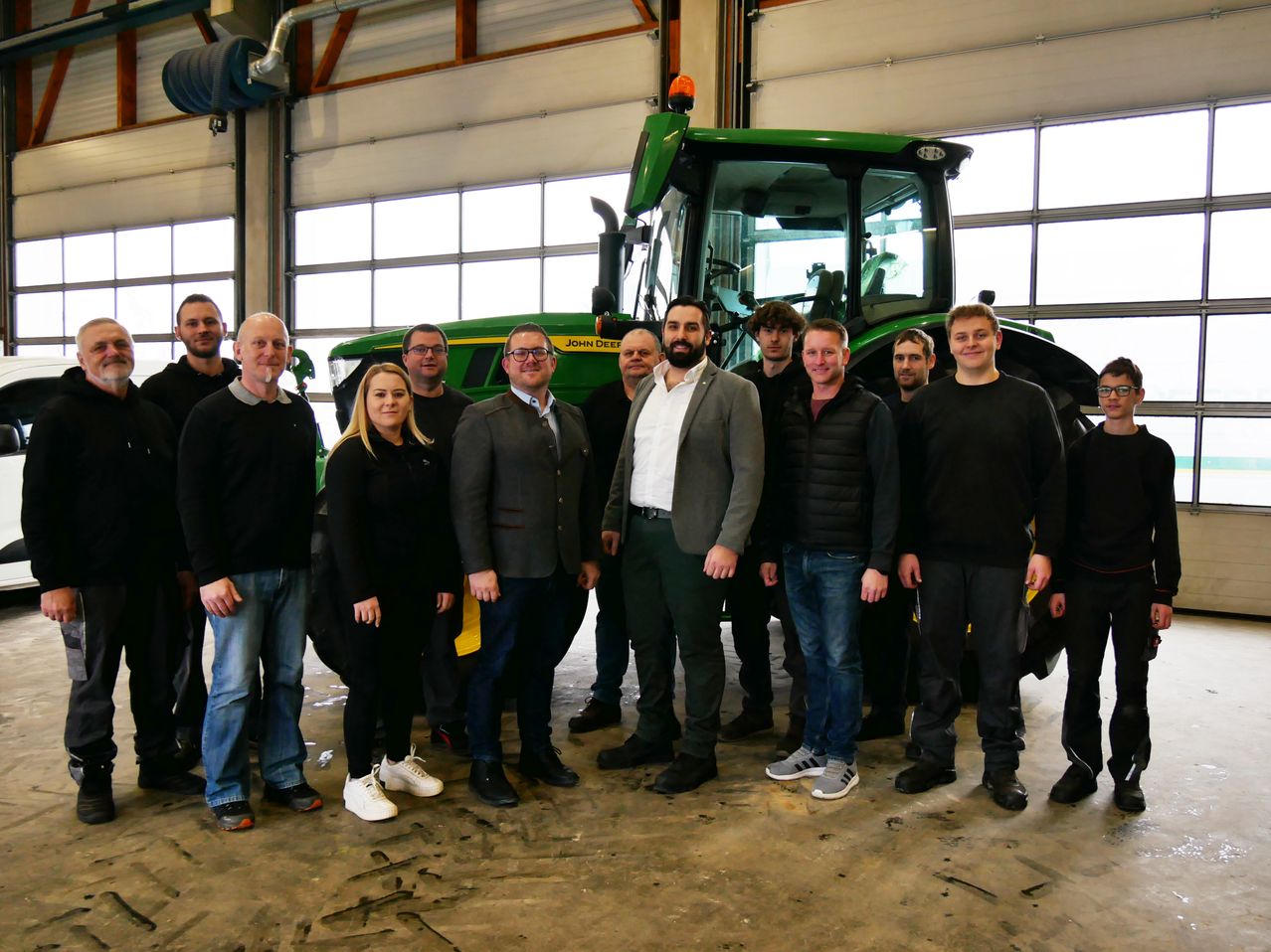 Eine Gruppe von Personen, darunter Männer und Frauen, steht vor einem John Deere Traktor in einer Garage.