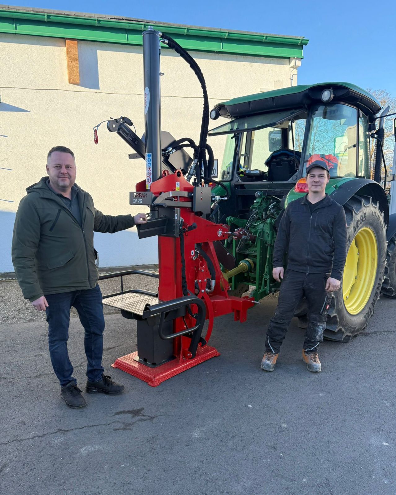 Zwei Männer stehen neben einem roten Traktor mit einer großen Anbauvorrichtung und posieren für ein Foto.